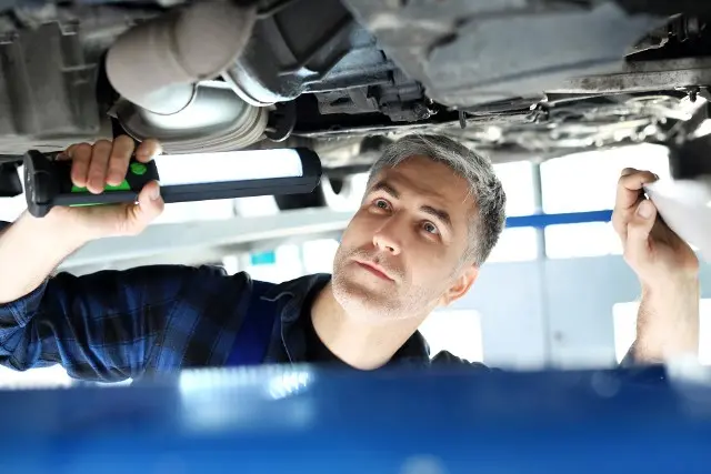 Mechaniker inspiziert Dieselpartikelfilter unter dem Fahrzeug